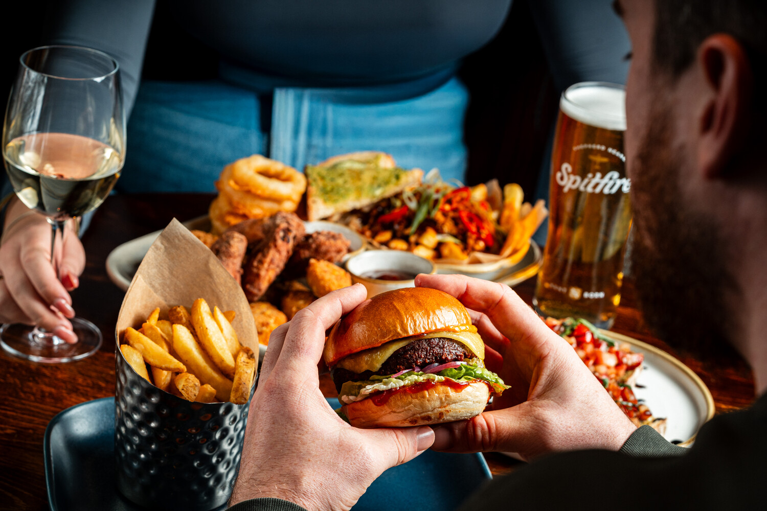 A man with food, wine and beer on the table, eating a burger and fries at the Sin Bin pub in Chatham.